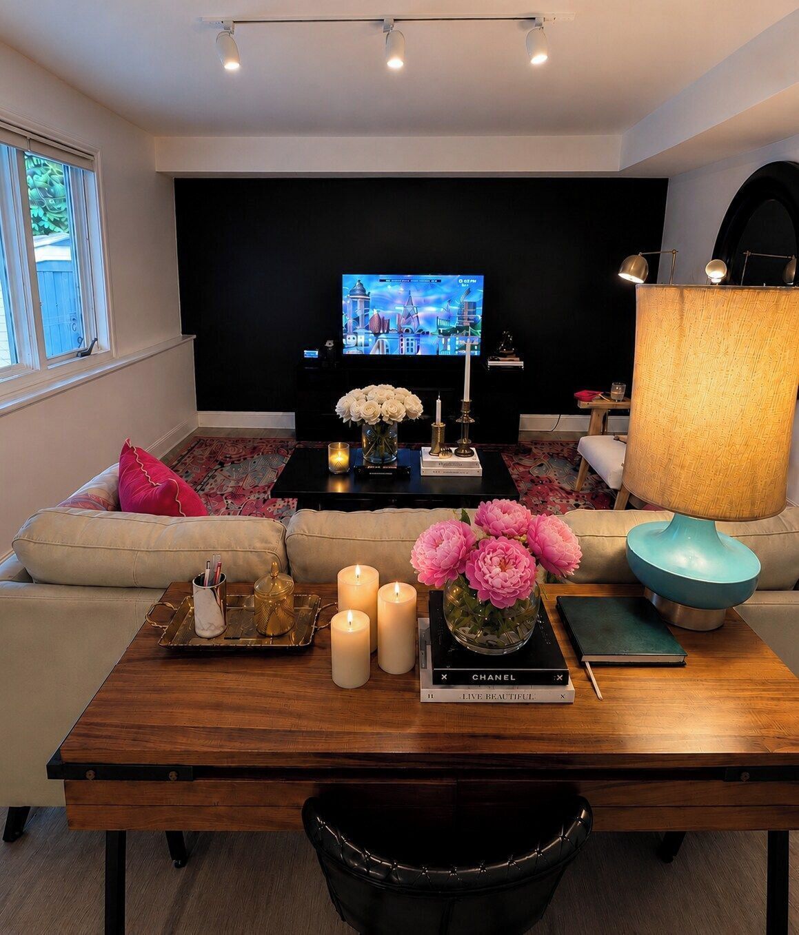 A modern living room with a flat-screen TV, a wooden coffee table with candles, flowers, and books, and a sofa with cushions.