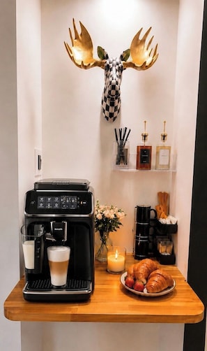 A coffee station with a coffee maker, cups, croissants, and a candle.