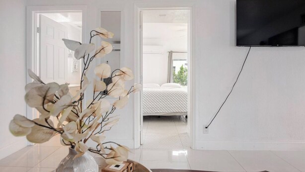 Ein modernes Zimmer mit einem großen Spiegel, einer Vase mit künstlichen Blumen, einer Fernbedienung und einem flachbildfernseher, der an der Wand befestigt ist.