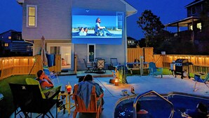 Ein Haus mit Sitzgelegenheit im Freien, einem Schwimmbad und einer großen Leinwand, auf der ein Film läuft.