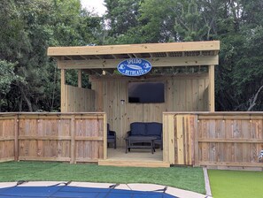A wooden outdoor structure with a sign reading 'SPEEDO RETREAT' and a flat-screen TV mounted on the wall.
