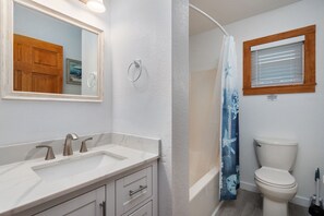 A bathroom with a white sink, two faucets, a mirror, a toilet, and a shower curtain.