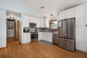 A modern kitchen with white cabinets, stainless steel appliances, and a wooden floor. - Just Wright: Heated Pool, Soundside, close to beach & sound! (Kitty Hawk)