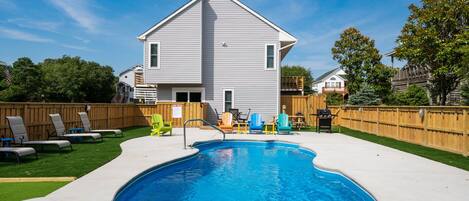 A residential backyard with a swimming pool, a wooden deck, and a house with a gabled roof.