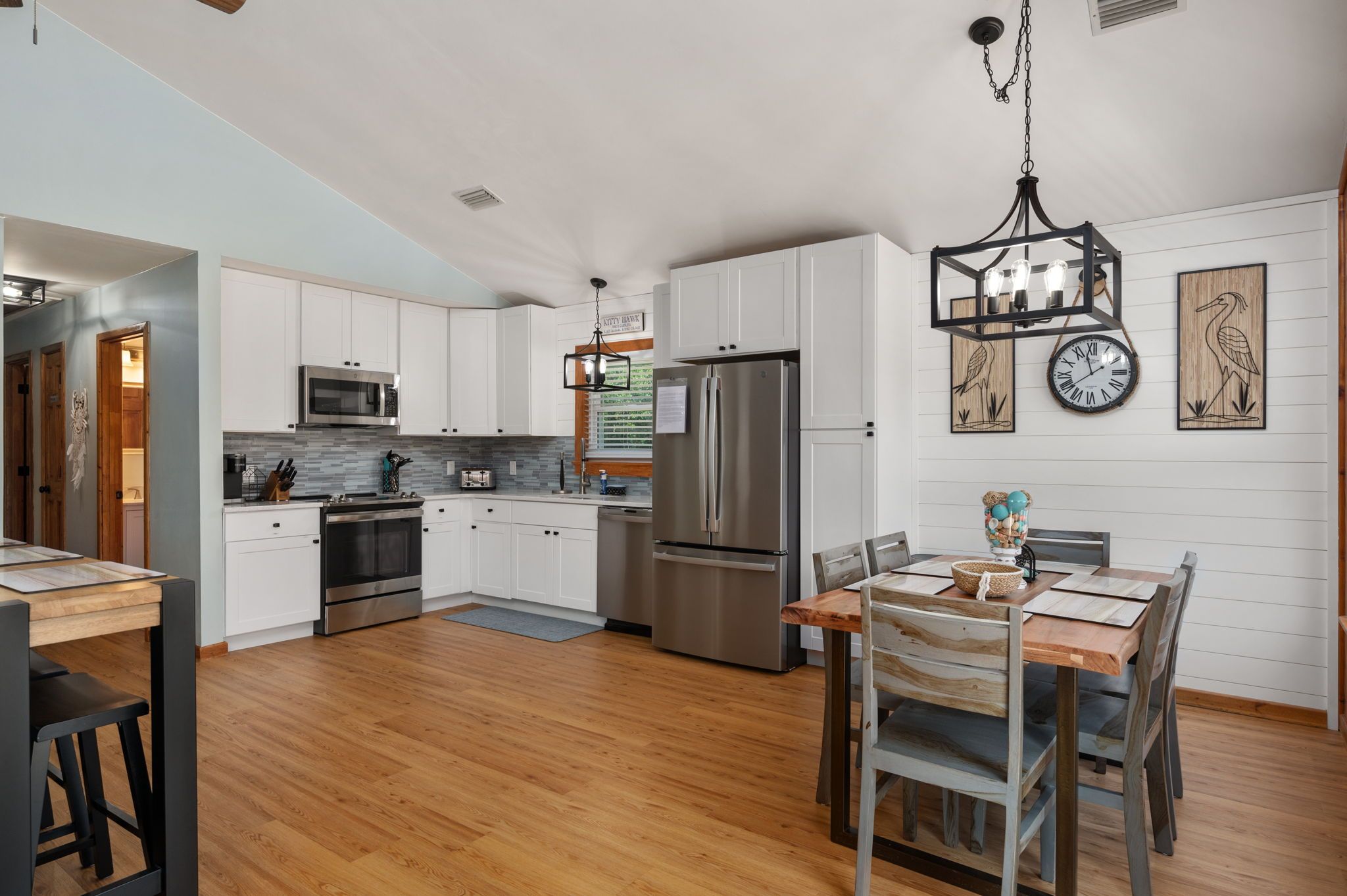 Una cocina moderna con armarios blancos, electrodomésticos de acero inoxidable y una zona de comedor con mesa y sillas de madera.