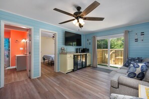 A spacious living area with a ceiling fan, a kitchen with a TV, and a sliding glass door to a deck.