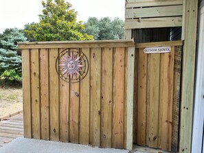 A wooden fence with a metal sun decoration and a sign reading 'OUTDOOR SHOWER'. - Just Wright: Heated Pool, Soundside, close to beach & sound! (Kitty Hawk)