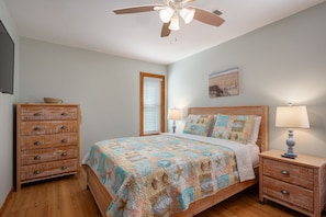 A bedroom with a wooden bed, a nightstand, a dresser, a ceiling fan, and a beach-themed wall art. - Just Wright: Heated Pool, Soundside, close to beach & sound! (Kitty Hawk)