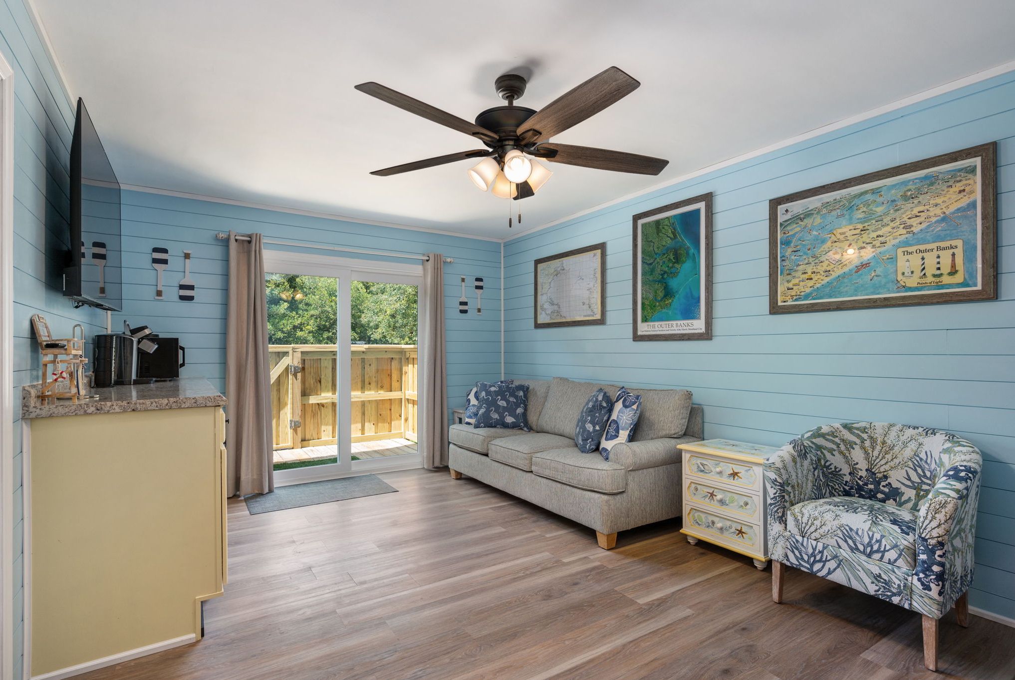 A room with a ceiling fan, a sofa, a patterned armchair, a small table, and a map on the wall.