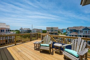 A wooden deck with Adirondack chairs and a view of beach houses.