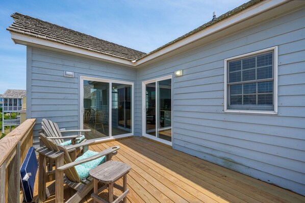 A covered deck with wooden furniture and sliding glass doors leading to an interior space.