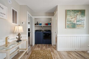 A laundry room with two washing machines, a rug, and a painting on the wall.