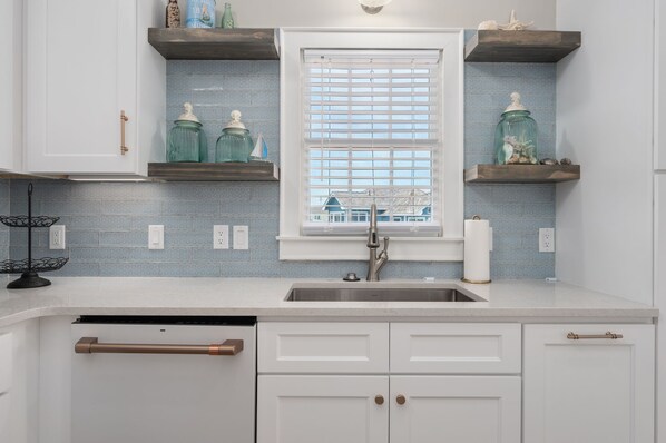 A kitchen with a window, built-in shelves, a sink, and a dishwasher.