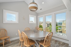 A dining room with a round table, wooden chairs, and large windows offering a view of the neighborhood.