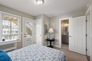 A bedroom with a bed, a nightstand, a lamp, and a door leading to a bathroom.
