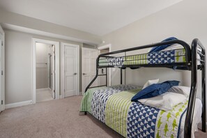 A single bunk bed with a patterned bedspread and pillows, a white door, and a carpeted floor.