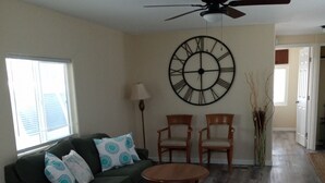A living room with a green sofa, two wooden chairs, a round wooden table, a large wall clock, and a ceiling fan. - Charm remodeled 2b 2b with 2/p space only 7 minutes from down town (Tucson)