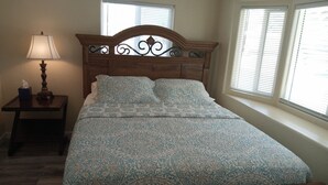 A neatly made bed with a patterned bedspread, a wooden headboard with decorative metalwork, a bedside table with a lamp, and windows with blinds. - Charm remodeled 2b 2b with 2/p space only 7 minutes from down town (Tucson)