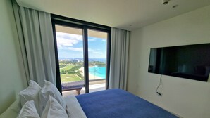Une chambre d’hôtel avec un grand lit, un téléviseur fixé au mur et un balcon offrant une vue sur la plage et l’océan.