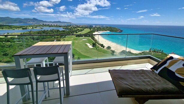 Un balcon avec une table et des chaises, donnant sur une plage et un terrain de golf.