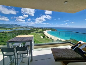 A balcony with a table and chairs, overlooking a beach and a golf course.