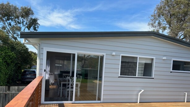 Ein Bungalow mit überdachter Terrasse, Schiebetür als Eingang und einem durch eine Zäunung abgegrenzten Deckbereich.