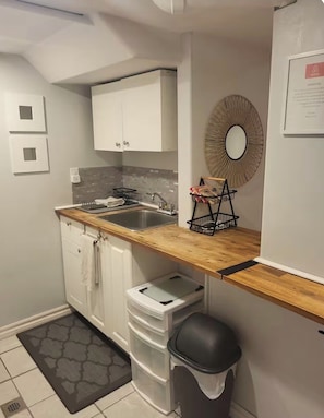 Une cuisine compacte dotée d’un plan de travail en bois, de meubles blancs, d’un évier, d’une poubelle et d’un miroir décoratif.