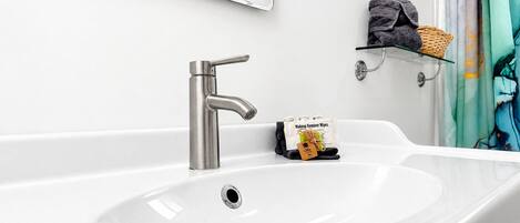 Un baño moderno con un lavamanos grande de color blanco, un grifo cromado, un espejo sobre el lavamanos y una repisa con artículos de aseo.