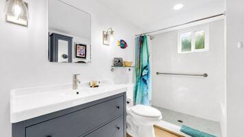 A modern bathroom with a white sink, dark vanity, a toilet, a shower with a glass door, and a small window.