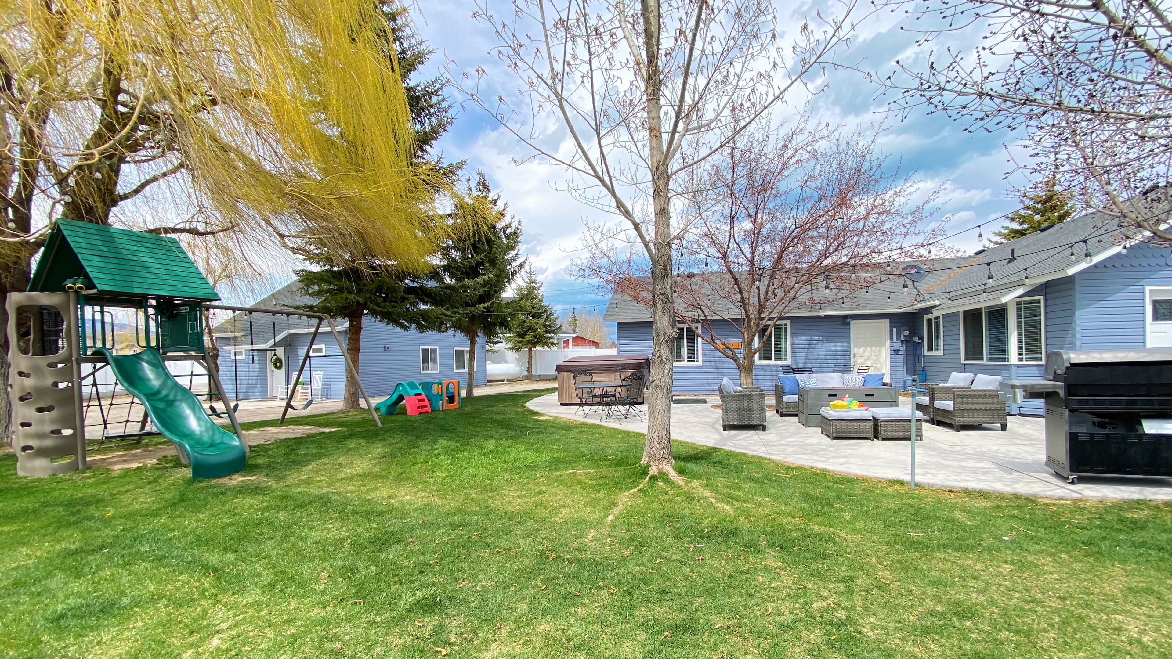 A backyard with a playground, outdoor seating, and a house.