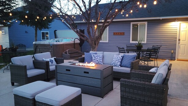 An outdoor patio with wicker furniture, a fire feature, and string lights.