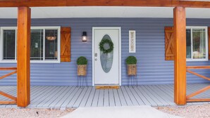 A house with a front porch, a white door, and two potted plants on either side.