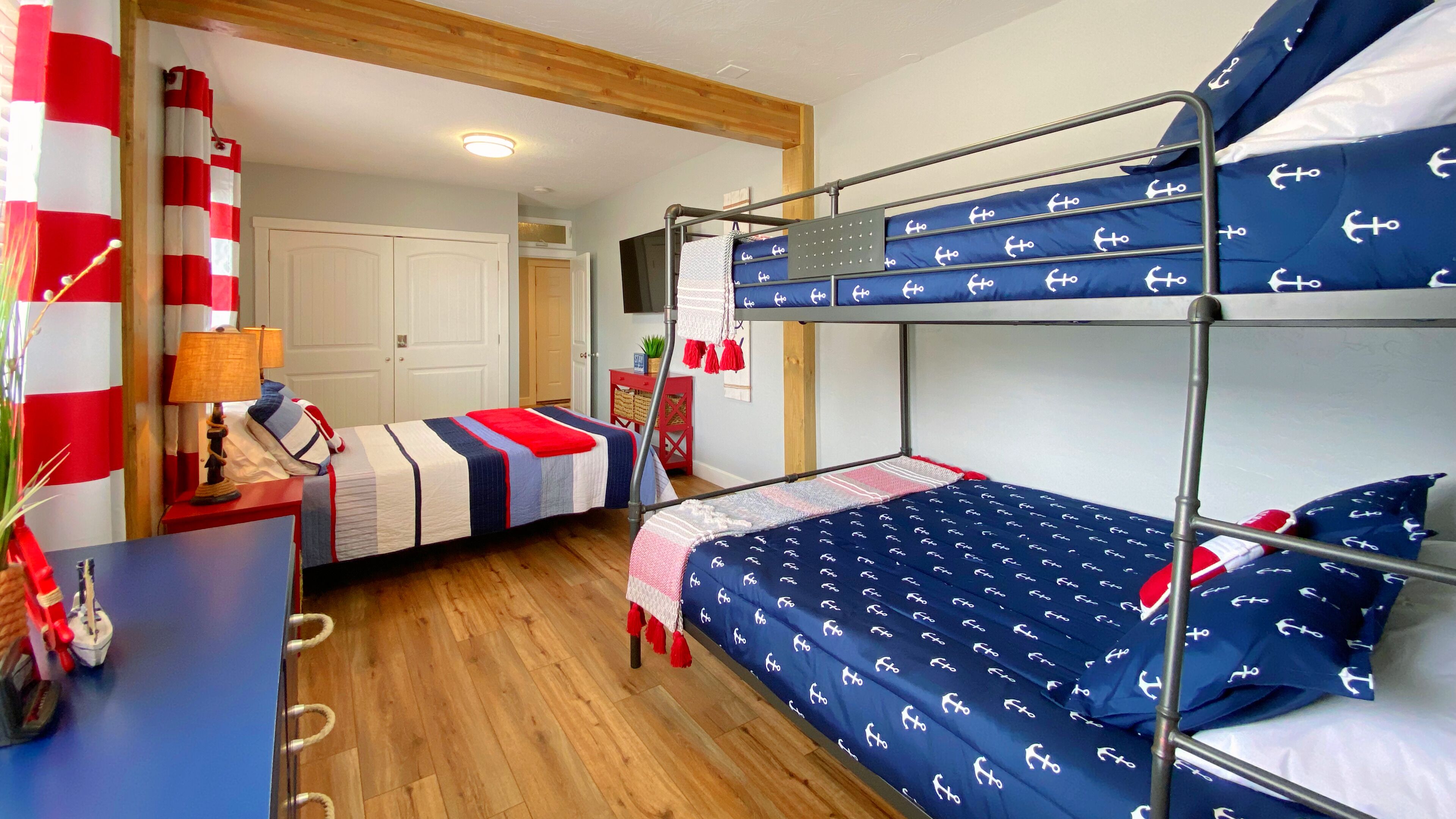 A bunk bed room with a nautical theme, featuring anchor-patterned bedding and red and white striped curtains.