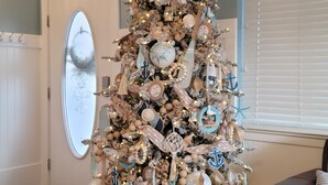 A beach-themed Christmas tree with nautical decorations, a sign reading "beach house," and a cozy seating area with a leather couch.