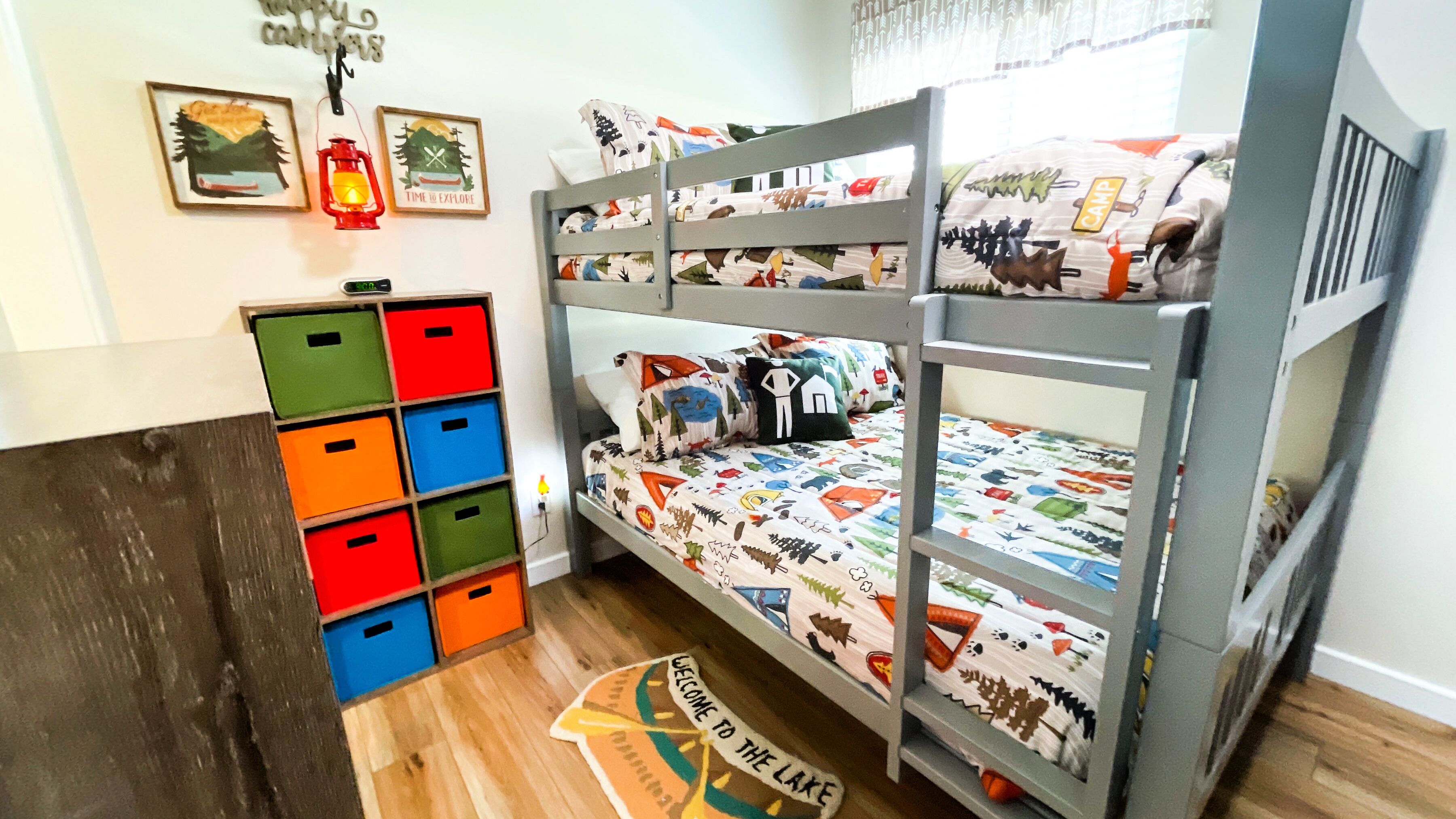 A bunk bed with colorful bedding, a small desk with a chair, and storage boxes.