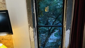 A rustic room with a round table, a white chair, and a wooden chair. A window with peeling paint offers a view of trees. - UP ON MAIN - a charming historic apartment in the heart of Eureka Springs (Eureka Springs)