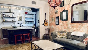 A kitchen with a central island, stools, and a dining table. There is a sofa with cushions and a mirror on the wall. - UP ON MAIN - a charming historic apartment in the heart of Eureka Springs (Eureka Springs)