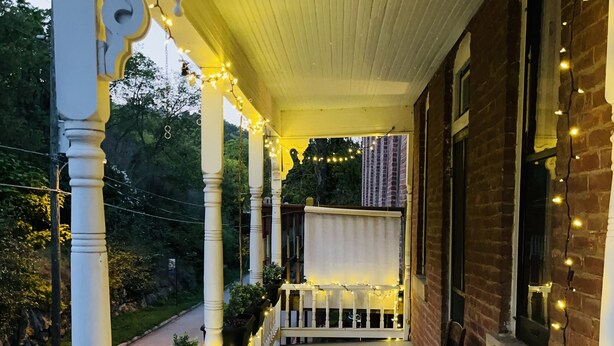 A porch with white balustrades, string lights, and potted plants. - UP ON MAIN - a charming historic apartment in the heart of Eureka Springs (Eureka Springs)