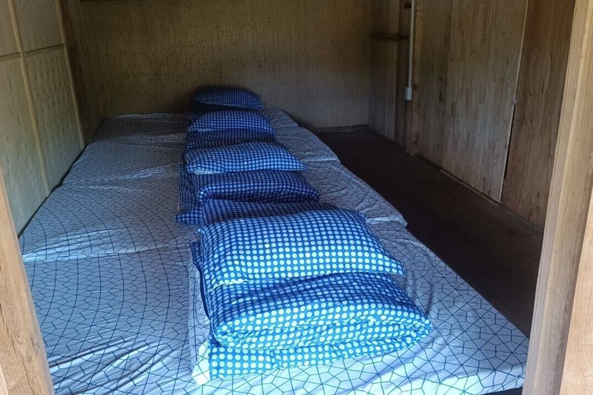 Ein schmales Zimmer mit einem Bett, das mit gemusterten Textilien bezogen ist.