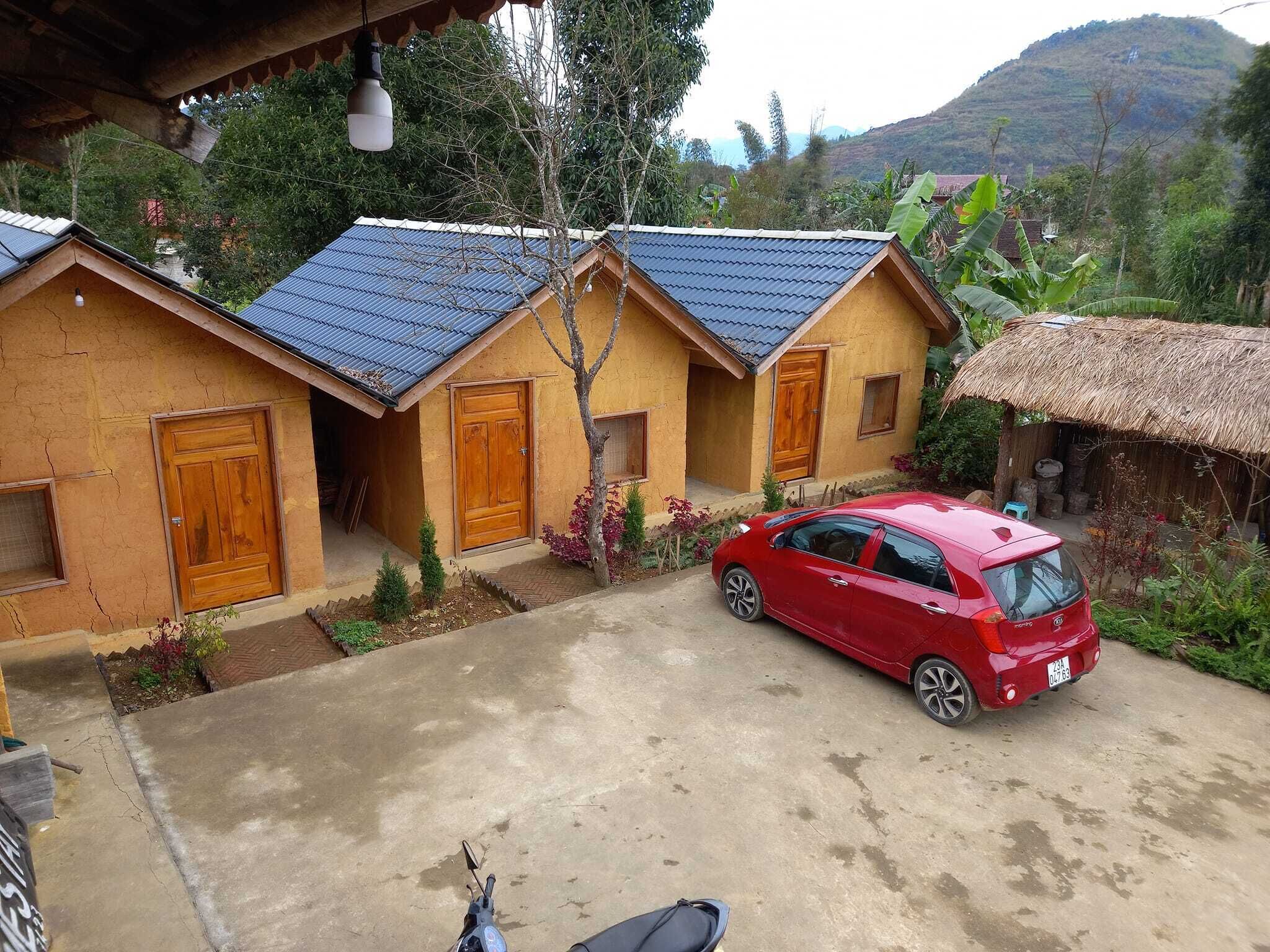 A red car parked in front of a building with a thatched roof and a blue-tiled roof.