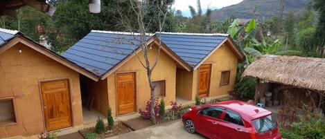 A red car parked in front of a building with a thatched roof and a blue-tiled roof.