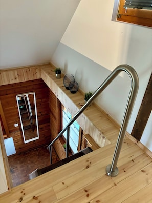 A wooden staircase with a metal handrail, a small plant on the landing, and a view of the lower level.
