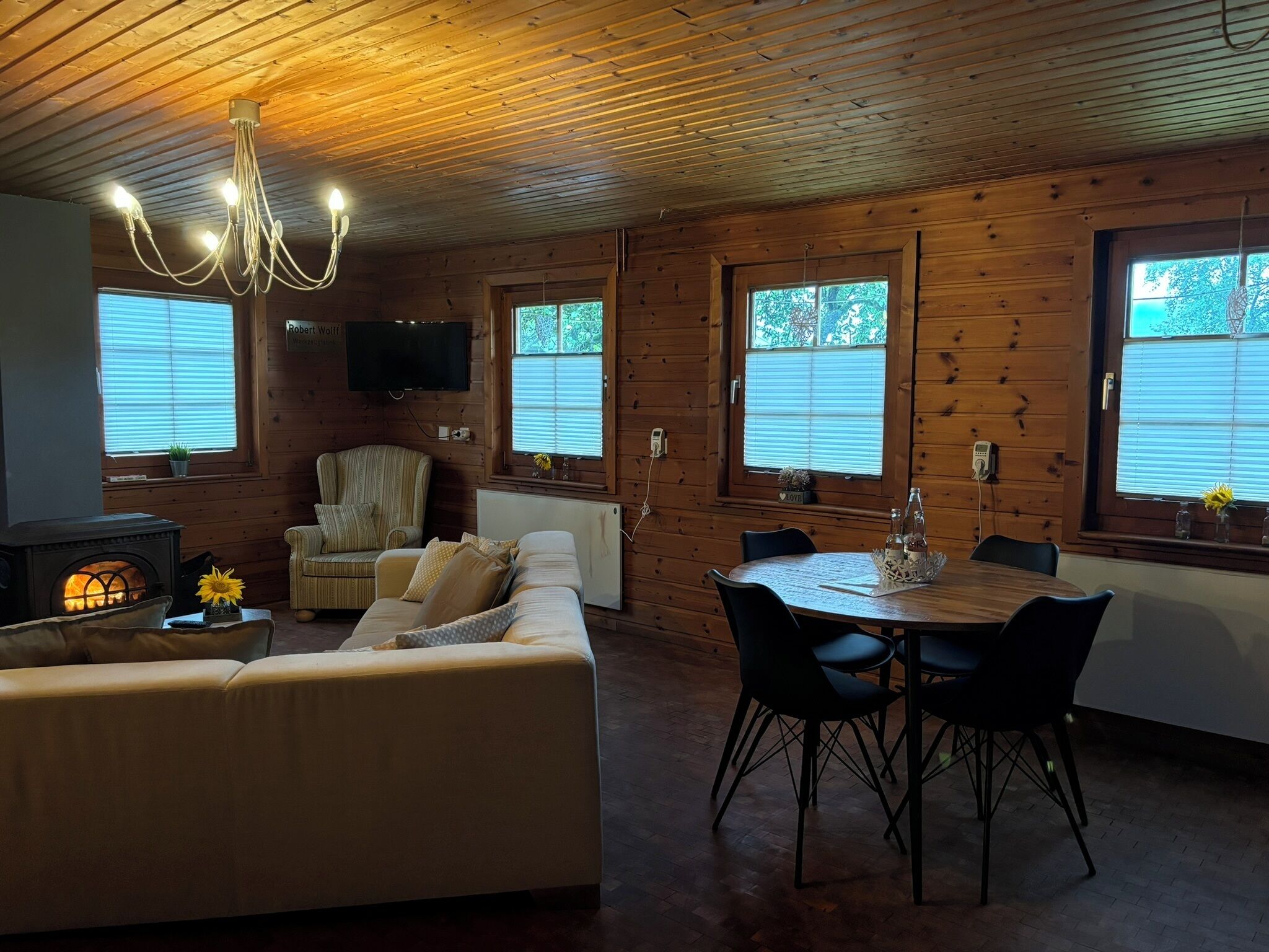 Un intérieur de chalet chaleureux avec un canapé, une table à manger, des chaises, un téléviseur et un poêle à bois.
