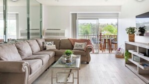 A living room with a sofa, a coffee table, a TV, and a balcony with outdoor furniture.