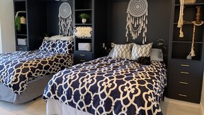 A modern bedroom with two beds, a dark wardrobe, decorative dreamcatchers, and a small plant.