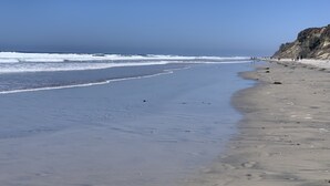A beach with a clear sky, waves, and a rocky cliff.