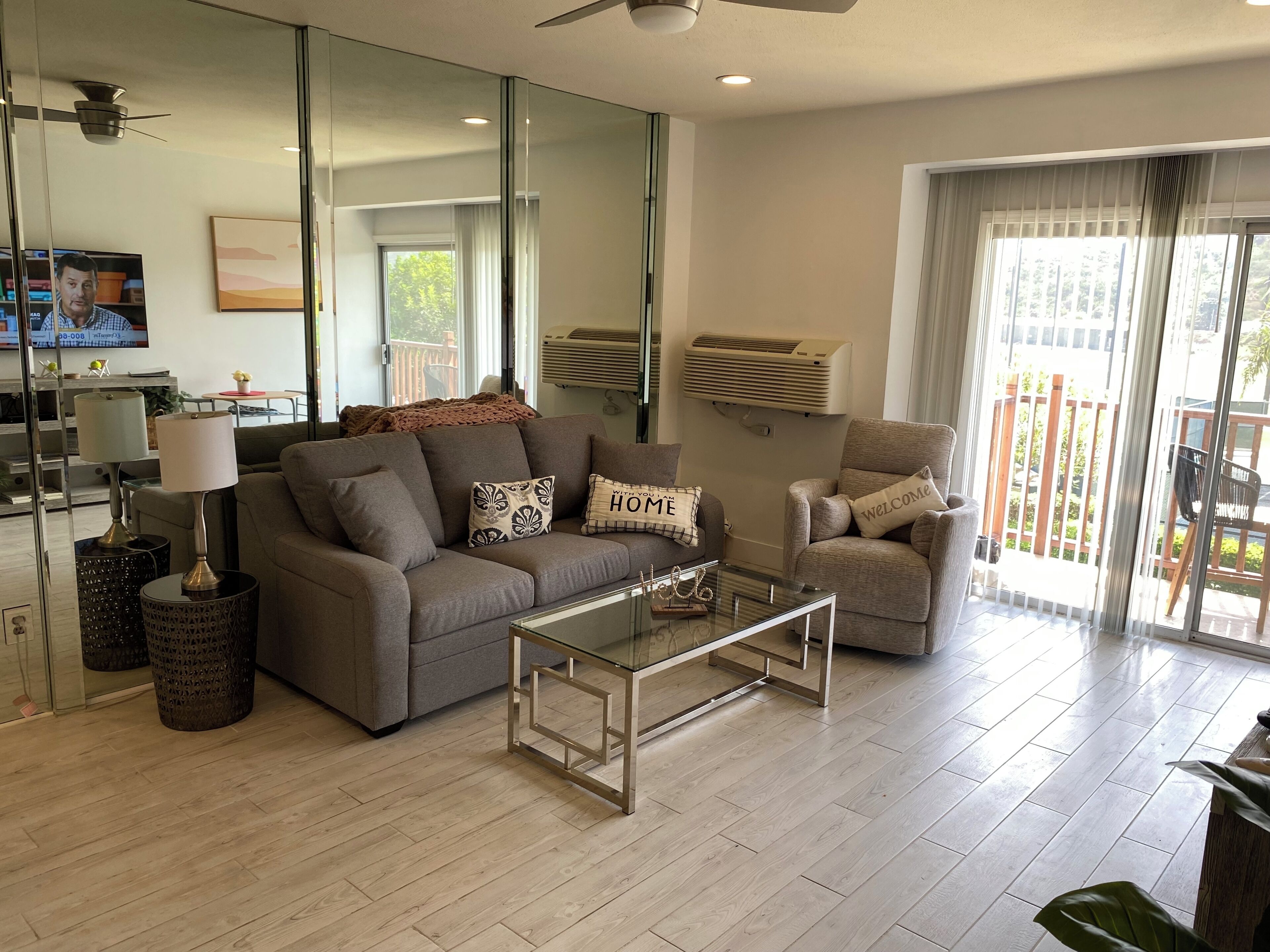 A modern living room with a sofa, armchair, glass coffee table, and a TV.