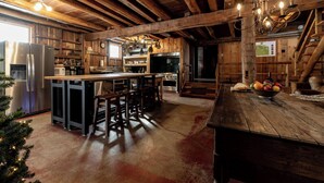 A rustic kitchen with wooden beams, a stainless steel refrigerator, a stove, and a wooden island with bar stools. - Beautifully Restored Five Bedroom 1860 Barn (Metamora)