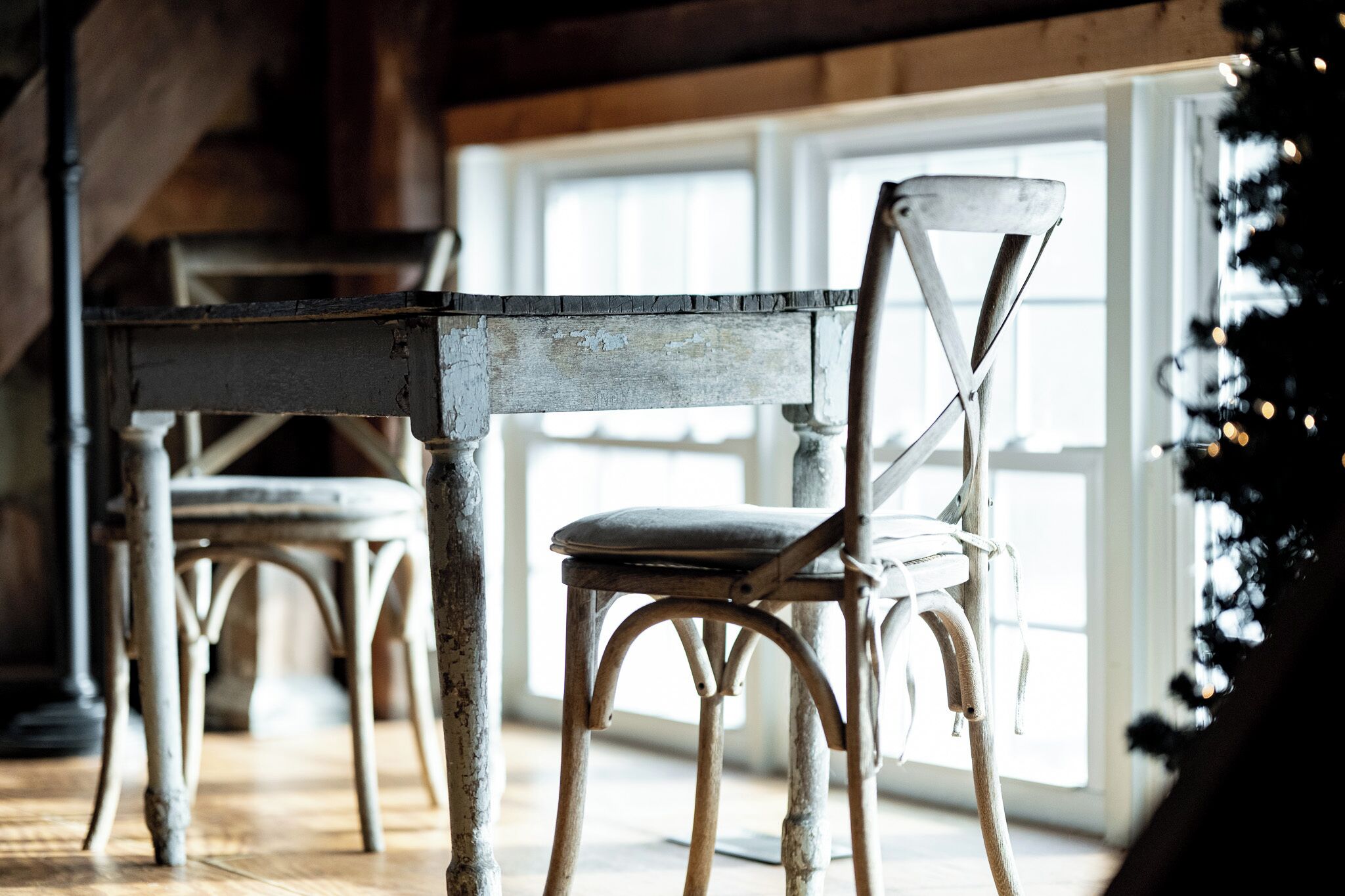 A rustic interior with a wooden dining table and chairs, a window with natural light, and a Christmas tree.
