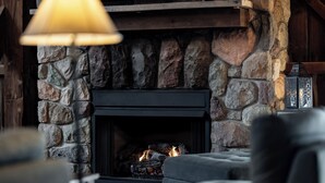 A stone fireplace with a black surround, a hanging lamp, and a cushioned seating area in front.